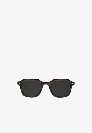 Schildkrötensonnenbrille mit dunklen Gläsern, quadratischen Fassungen und einem leicht erhöhten Augenbrauenbalken. Besitzt ein kleines Logo an der Seite.