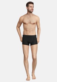 Black boxer shorts made of fabric with green stitching accents, featuring a fitted shape, elastic waistband, and no visible logos.