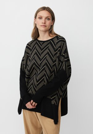 Maglione nero con un motivo a zigzag dorato, dotato di maniche lunghe e spacchi laterali. Tessuto morbido con una vestibilità comoda. Abbinato a pantaloni beige.