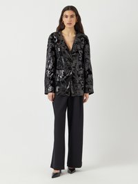 Blazer noir à sequins avec motif floral, décolleté en V profond, fermeture par bouton et manches longues. Associé à un pantalon noir ajusté et des escarpins à bout pointu.