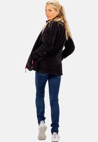Schwarze Fleecejacke mit lässiger Passform, ausgestattet mit pinken Reißverschlussakzenten und seitlichen Taschen. Getragen mit blauen Jeans und weißen Sneakers.