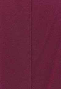 Lähikuva viininpunaisesta neuloksesta, jossa on keskellä pystysuora sauma.