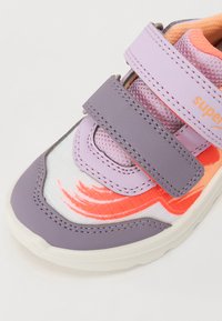 Lilla ja oranž spordijalats Velcro rihmadega, kangast ülemine osa, millel on abstraktsed mustrid, ja tekstuuriga talla, et tagada haardumine.