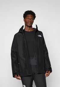 Schwarze wasserfeste Jacke mit Kapuze, ausgestattet mit einem Reißverschluss auf der Vorderseite und dem Logo von The North Face auf der Brust. Lockere Passform und strukturierter Stoff.