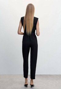 Černý overal s upnutým pasem, bez rukávů, se zúženými nohavicemi a hladkou strukturou. Obsahuje pásek v pase a uzavřené podpatky.