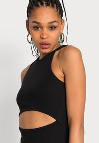 Camisola cropped preta com uma gola alta e detalhes recortados nas laterais, apresentando alças largas e uma silhueta justa.