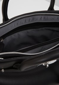 Schwarze Lederhandtasche, geöffnet, zeigt graues Stofffutter mit zwei Reißverschlussfächern und runden Griffen.