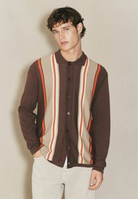 Brauner Button-Up Cardigan mit vertikalen Streifen in Orange, Beige und Creme. Weicher Stoff, Kragen-Design und lockerer Schnitt.