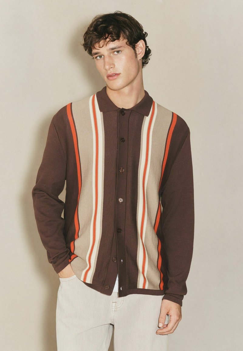 Cardigan marrone con bottoni, caratterizzato da righe verticali in arancione, beige e crema. Texture morbida, design con colletto e vestibilità rilassata.