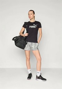 Svart Puma-t-shirt med silvrig logotyp, mönstrade grå shorts, svarta sneakers med rosa detaljer och en svart sportväska. Vita strumpor.