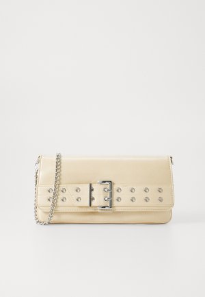 Beżowa torebka kopertówka z szerokim paskiem z metalowymi oczkami i klamrą, oraz srebrnym łańcuszkiem na białym tle.