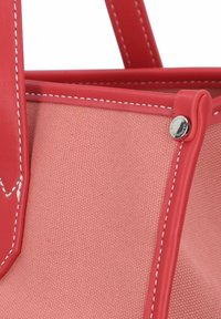 Röd läder- och rosa canvas toteväska med vit sömnad, utrustad med en metalldetalj och en strukturerad design. Handtagen är robusta och integrerade.