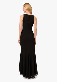 Abito da sera nero con corsetto aderente e gonna svasata. Il design senza maniche presenta un'apertura a forma di chiave sul retro e una leggera trasparenza all'orlo.