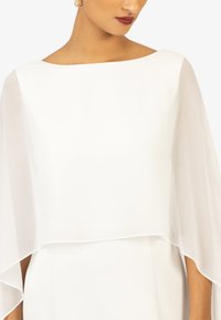 White dress featuring a flowing, sheer overlay with a rounded neckline and soft, lightweight texture, creating an elegant drape.