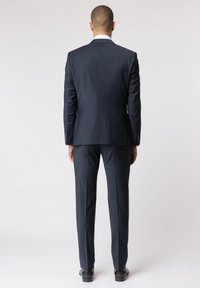 Marineanzug mit taillierter Passform, ausgestattet mit einem einzelnen Schlitz am Rücken und passenden Hosen. Abgerundet mit eleganten schwarzen Schuhen.