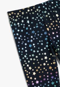 Leggings negras con un patrón de estrellas metálicas en varios colores, con una cinturilla elástica y una textura de tela suave y lisa.
