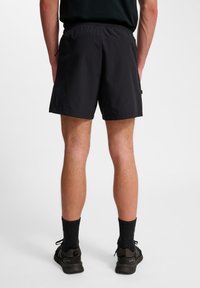 Schwarze Sportshorts mit einem Kordelzugbund, glatter Textur und geradem Schnitt. Sichtbare Taschen auf der Rückseite und minimaler Markenaufdruck.