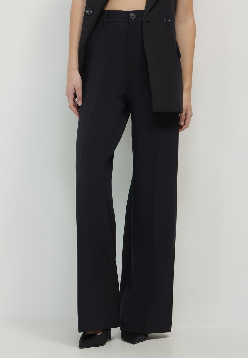 Pantalons noirs à jambes larges en tissu lisse, avec une taille haute et des lignes épurées, dotés de plis avant et sans motifs visibles.