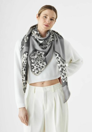 Grijze en witte sjaal met een patroon van luipaardprint en dierenmotieven, in een driehoekige vorm en met een zachte textuur, gedragen over een witte crop sweater.