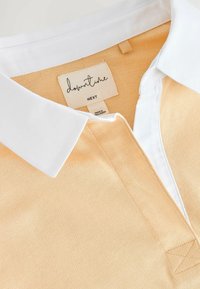 Polo shirt with a white collar, featuring a light orange textured body and a tag reading "downtime" under the collar.