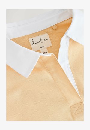 Polo tričko s bílým límcem, má světle oranžové strukturované tělo a štítek s nápisem "downtime" pod límcem.