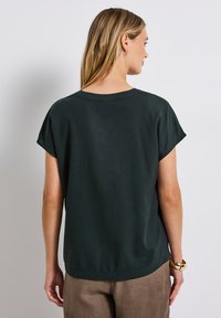 Dunkelgrüne Bluse mit kurzen Ärmeln und runder Ausschnitt, aus weichem Stoff und in lässiger Passform. Mit einem gesäumten Saum am unteren Ende.