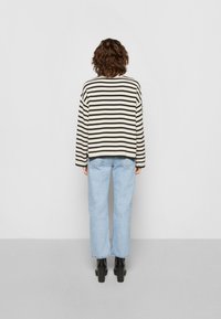 Pull rayé noir et crème, coupe décontractée, associé à un jean bleu clair à jambes droites. Des bottines noires à talons complètent la tenue.