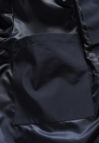 Marineblauwe satijnen stof met een gladde textuur, voorzien van een vierkante zak. Het oppervlak heeft een subtiele glans en geen zichtbare patronen.