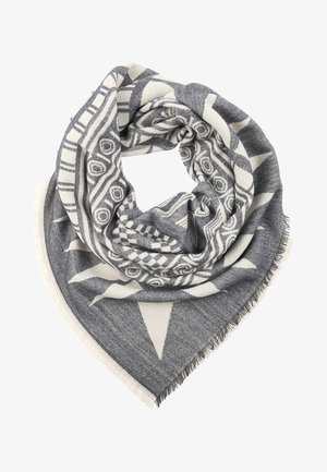 Foulard carré avec des motifs tribaux géométriques noirs et blancs, des bords à franges asymétriques et un tissu tissé doux, disposé en forme de spirale de manière lâche.