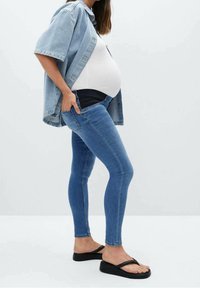 Jeans skinny de maternidad en denim azul claro, con una cinturilla cómoda y piernas ajustadas. Combinados con una blusa blanca y una camisa de denim.