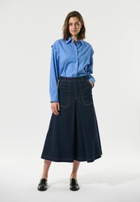  lichtblauw gestreept overhemd met lange mouwen, gecombineerd met een donkere denim A-lijn rok met voorzakken en contrasterende stiksels.