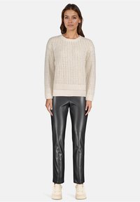Beżowy sweter dziany z otwartym wzorem, okrągły dekolt; połączony z czarnymi spodniami z sztucznej skóry i kremowymi sneakersami.