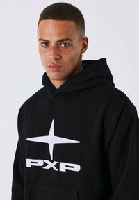Zwarte hoodie met een witte sterlogo en "PXP" tekst op de voorkant. De stof lijkt zacht, met een relaxte pasvorm en een voorzakdetail.