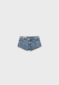 Shorts en denim bleu avec ourlets effilochés, décorés de clous métalliques uniformément espacés, présentés sur un fond gris clair uni.