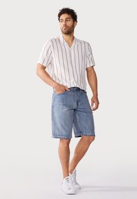 Witte kortelange mouwen shirt met bruine verticale strepen, gecombineerd met blauwe denim shorts en witte sneakers. Heeft een knoopsluitingen ontwerp en een relaxte pasvorm.