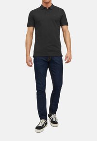 Sort polo shirt med krave, parret med mørkeblå jeans og sorte sneakers. Skjorten har et lille logo på brystet.