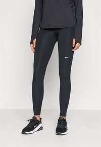 Black athletic leggings with a smooth texture and a fitted design, featuring a small white Nike logo on the upper leg. Paired with black sneakers.