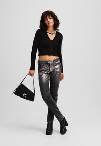 Černý žebrovaný crop top s knoflíky, metalicky šedé džíny a černá trojúhelníková taška s logem, doplněné černými platformovými botami.