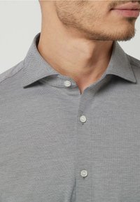 Grau kurzes T-Shirt mit subtiler Textur, einem klassischen Kragen und zwei sichtbaren weißen Knöpfen am Halsausschnitt.