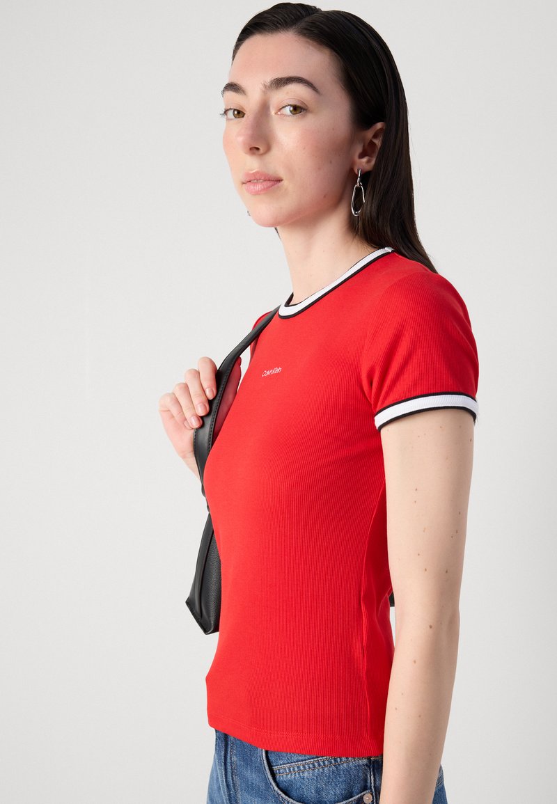 Camiseta roja de canalé con ribete blanco en el cuello y las mangas. Diseño ajustado, mangas cortas y un pequeño logo en el pecho.