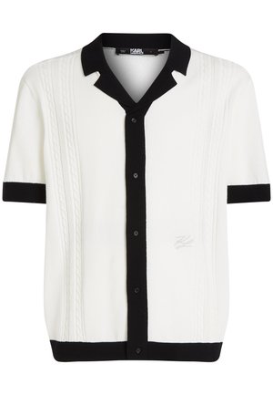 Short-sleeve knit shirt in white with black collar and button placket, featuring cable knit patterns along the front and a logo detail.