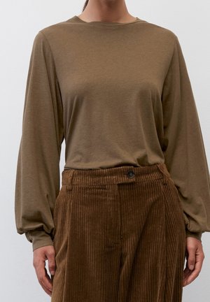Personne portant un haut marron à manches longues et un pantalon en velours côtelé marron foncé taille haute avec une fermeture à boutons.