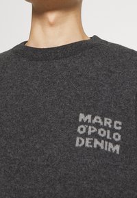 Dunkelgrauer Strickpullover mit Rundhalsausschnitt, der ein weißes, pixeliertes Logo "MARC O'POLO DENIM" auf der Brust trägt. Weicher Stoff.