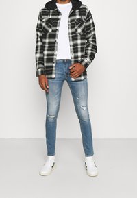 Svart och vit rutig flanellskjorta med svart huva, vit crew neck t-shirt, slitna ljusblå jeans, vita sneakers.