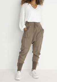 Beige cargobyxor med elastisk midja, sidofickor och ankle ties. Matchas med en vit långärmad topp och vita sneakers.