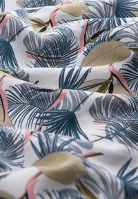 Tissu en coton présentant un motif de feuilles tropicales dans des tons de vert foncé, bleu, rose et beige sur fond blanc, avec une texture douce et lisse.