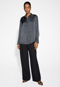 Camicia a maniche lunghe con bottoni in satin grigio scuro, abbinata a pantaloni neri a gamba larga e sandali neri con punta aperta.