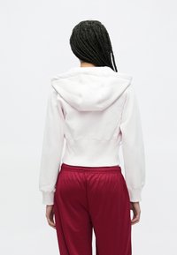 Biela skrátená mikina s kapucňou, rebrovanými manžetami, v kombinácii s voľnými vínovými teplákmi s elastickým pásom.