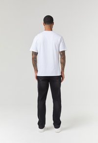 Camiseta blanca de algodón con escote redondo, mangas cortas y corte relajado, combinada con jeans de mezclilla negros y zapatillas blancas.
