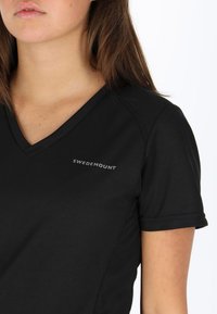 T-shirt nera a maniche corte con scollo a V realizzata in un tessuto liscio, caratterizzata da un logo "SWEDEMOUNT" sulla parte sinistra del petto, trasmettendo un design casual.
